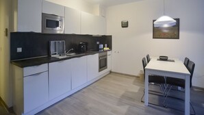 A modern kitchen with white cabinets, a microwave, a coffee maker, and a dining table with chairs. - Comfort apartment with 1 bedroom and terrace on the first floor (Ostseebad Binz)