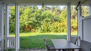 A covered patio with a table and chairs, a view of a grassy yard and trees. - Comfort apartment with 1 bedroom and terrace on the first floor (Ostseebad Binz)