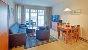 A modern living room with a sofa, armchairs, a coffee table, and a dining area with a table and chairs. - Comfort apartment with 1 bedroom and balcony on the upper floor (Ostseebad Binz)
