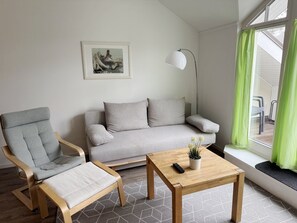 A living room with a grey sofa, a grey armchair, a wooden coffee table, and a floor lamp. - Komfortplus Ferienwohnung mit 1 Schlafzimmer und Balkon im Dachgeschoss (Ostseebad Binz)