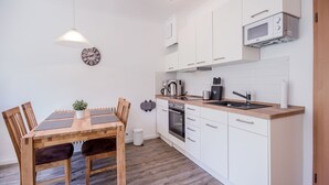 Ett modernt kök med vita skåp, en bänkskiva i trä och en inbyggd ugn. Här finns ett matbord med stolar och en hängande lampa.