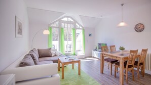 Ett modernt vardagsrum med en vit soffa, ett matbord med stolar och en grön matta.
