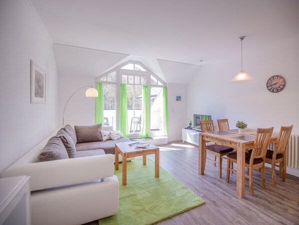 Un salon moderne avec un canapé blanc, une table à manger avec des chaises et un tapis vert.