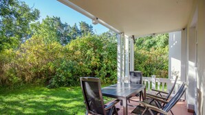 An outdoor patio with a table and chairs, surrounded by greenery and a white fence. - Comfortplus vacation apartment with 1 bedroom and terrace on the first floor (Ostseebad Binz)