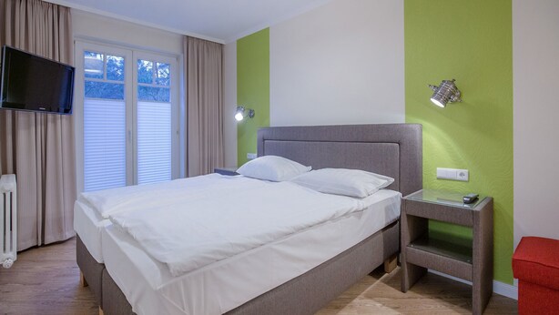A bedroom with a bed, a TV, a bedside table, and a red bench. - Comfortplus vacation apartment with 1 bedroom and terrace on the first floor (Ostseebad Binz)