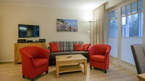 A living room with a sofa, two armchairs, a coffee table, a TV, and a painting on the wall. - Comfortplus vacation apartment with 1 bedroom and terrace on the first floor (Ostseebad Binz)