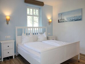 Une chambre à coucher avec un lit blanc, deux tables de chevet, une fenêtre et un tableau au mur.