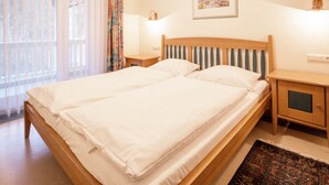 Een netjes opgemaakt bed in een hotelkamer, met een houten hoofdbord, een nachtkastje met een lamp en een ingelijste foto aan de muur.