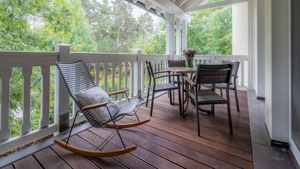 Una terraza de madera con barandilla blanca, una mecedora y una mesa con sillas.