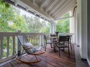 Une terrasse en bois avec une balustrade blanche, une chaise berçante et une table avec des chaises.