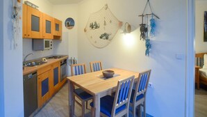 A compact kitchen with wooden cabinets, a microwave, and a dining area with a wooden table and blue chairs. - Comfort apartment with 1 bedroom and balcony on the top floor (Ostseebad Binz)