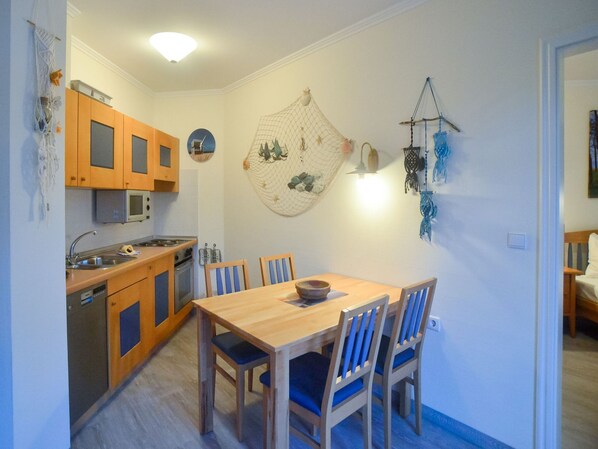 Ett kompakt kök med träskåp, en mikrovågsugn och en matplats med ett träbord och blå stolar.