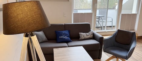 A living room with a sofa, a coffee table, a chair, a floor lamp, and a window with blinds.