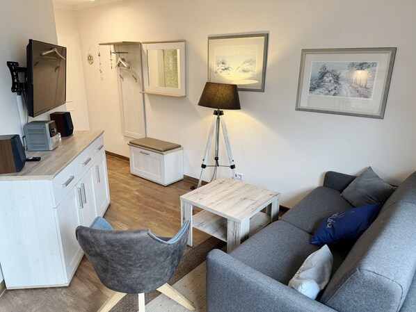 A modern living room with a grey sofa, a small white table, a grey armchair, a desk with a computer and speakers, a floor lamp, and framed artwork on the walls. - Comfort Apartment with 1 bedroom and a balcony on the top floor (Ostseebad Binz)