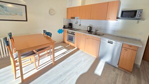 A compact kitchen with wooden cabinets, a microwave, a coffee maker, and a dishwasher. - Comfort apartment with 1 bedroom and balcony on the upper floor (Ostseebad Binz)