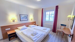 A hotel room with two beds, a desk, a chair, and a window with curtains. - Comfort apartment with 1 bedroom and balcony on the upper floor (Ostseebad Binz)