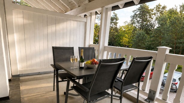 A covered patio with a table and chairs, a bottle of wine, and a bowl of fruit. - Comfort apartment with 1 bedroom and balcony on the upper floor (Ostseebad Binz)