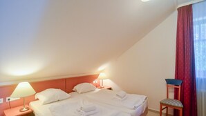 Ett hotellrum med två sängar, ett nattduksbord med en lampa, en stol och ett fönster med röda gardiner.