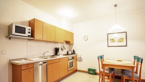 A compact kitchen with wooden cabinets, a microwave, a dishwasher, and a dining area with a table and chairs. - Comfort apartment with 1 bedroom and balcony on the upper floor (Ostseebad Binz)