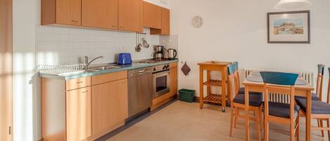 A modern kitchen with wooden cabinets, a dishwasher, and a dining area with a table and chairs.