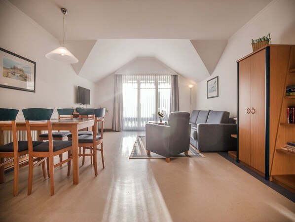 A spacious living area with a dining table, chairs, a sofa, and a wooden cabinet. - Comfort apartment with 1 bedroom and balcony on the top floor (Ostseebad Binz)