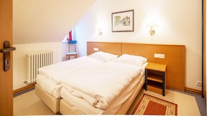 Un dormitorio con una cama grande, una mesita de noche, una silla, un radiador y un cuadro enmarcado en la pared.