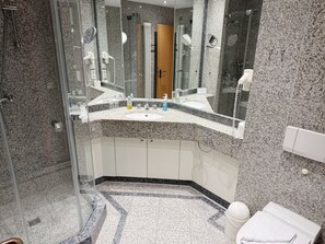 A modern bathroom with a granite countertop, a glass shower enclosure, and a white sink.