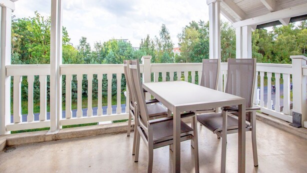Un patio cubierto con barandilla blanca, una mesa y cuatro sillas.
