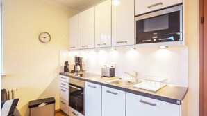 A compact kitchen with white cabinets, a built-in oven, a microwave, and a sink. - Comfort plus apartment with 1 bedroom and balcony on the top floor (Ostseebad Binz)