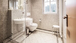 A bathroom with granite walls, a white sink, a toilet, a small stool, and a window with a view of trees. - Comfort plus apartment with 1 bedroom and balcony on the top floor (Ostseebad Binz)