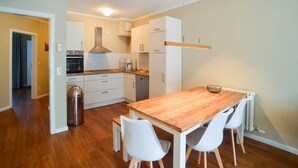 Una cocina moderna con armarios blancos, una mesa de comedor de madera y sillas blancas.