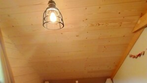 Een kleine, knusse slaapkamer op zolder met een schuine kap, een enkel bed met een wit en bruin dekbed, twee nachtlampjes en een hanglamp.