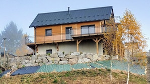 Een huis met twee verdiepingen, een stenen fundering, een balkon en een metalen dak.