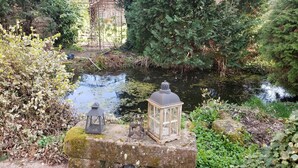 A serene garden with a pond, surrounded by lush greenery and two lanterns on a stone ledge. - GITE A LA PETITE FONTAINE-RDC  (Langensoultzbach)