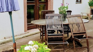 A patio with a table and chairs, a potted plant, and a door with an arched entrance. - GITE A LA PETITE FONTAINE-RDC  (Langensoultzbach)