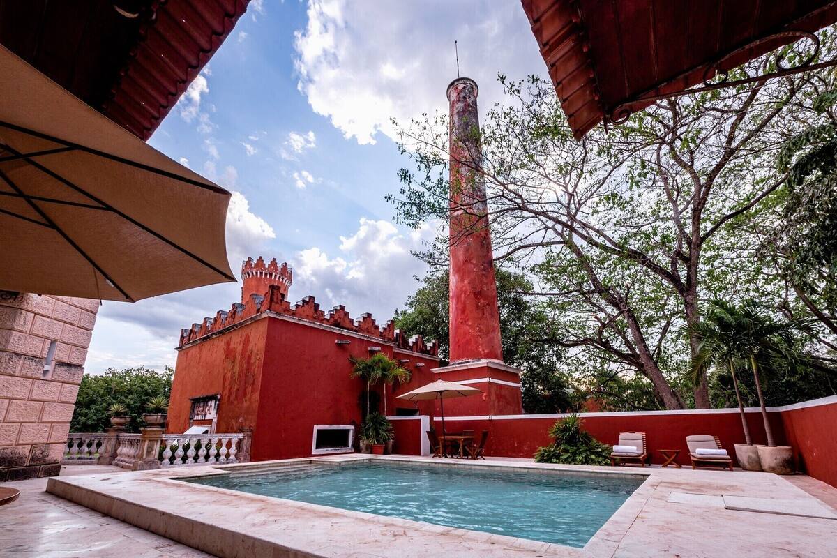 A pool area with a red building, a tall tower, and a palm tree.