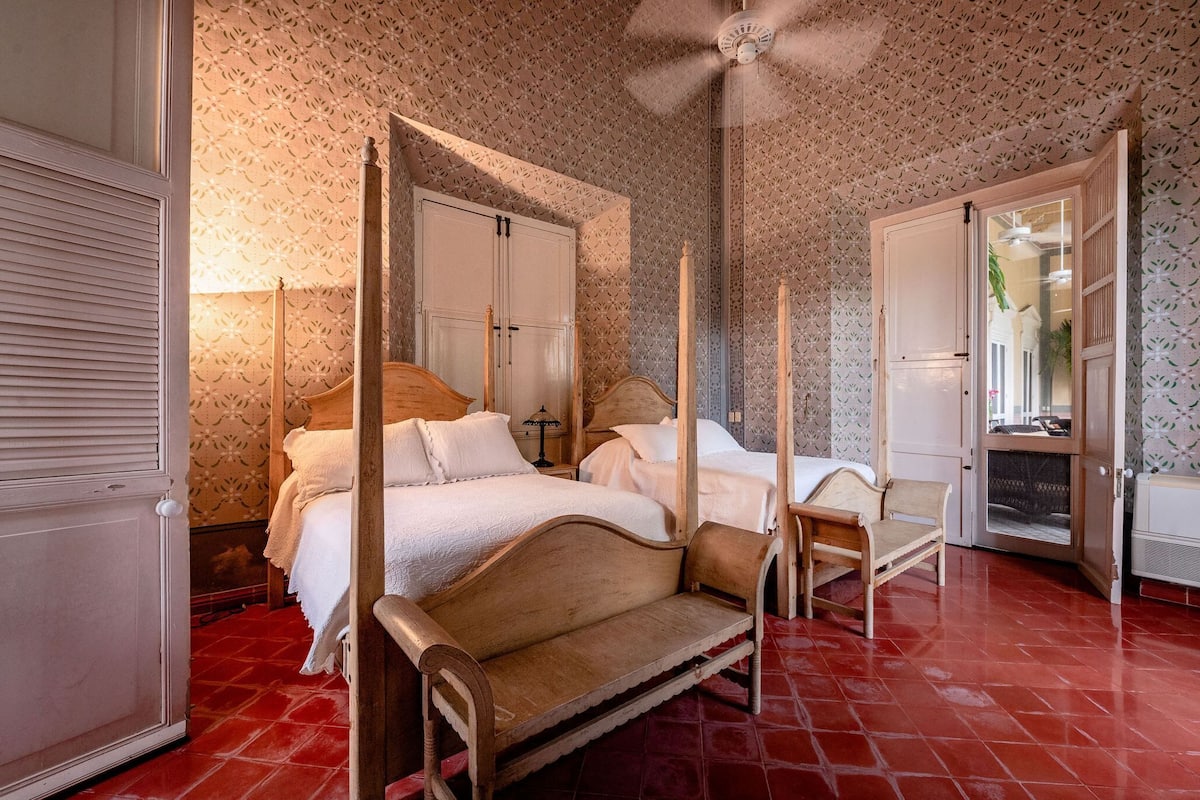 A four-poster bed with a wooden frame, a wooden bench, and a wardrobe with a mirror.