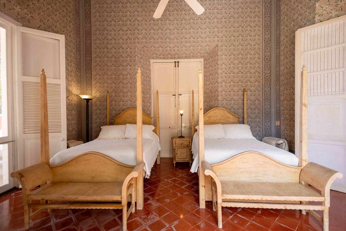 A room with two wooden four-poster beds, a small bedside table, and a nightstand.