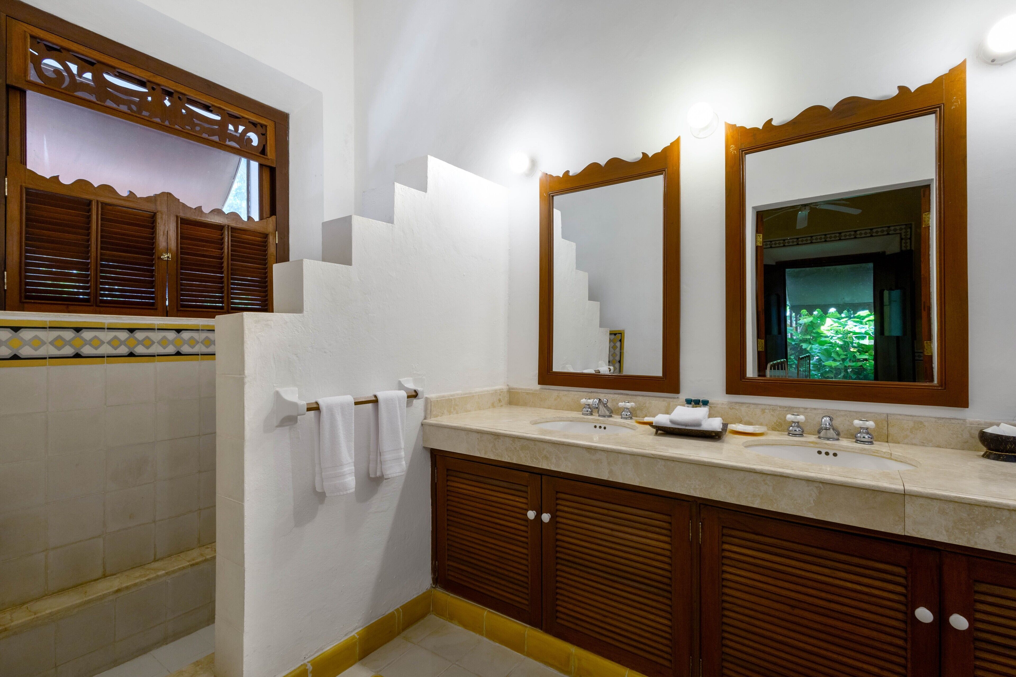 A bathroom with a sink, two mirrors, wooden cabinets, and a towel rack.