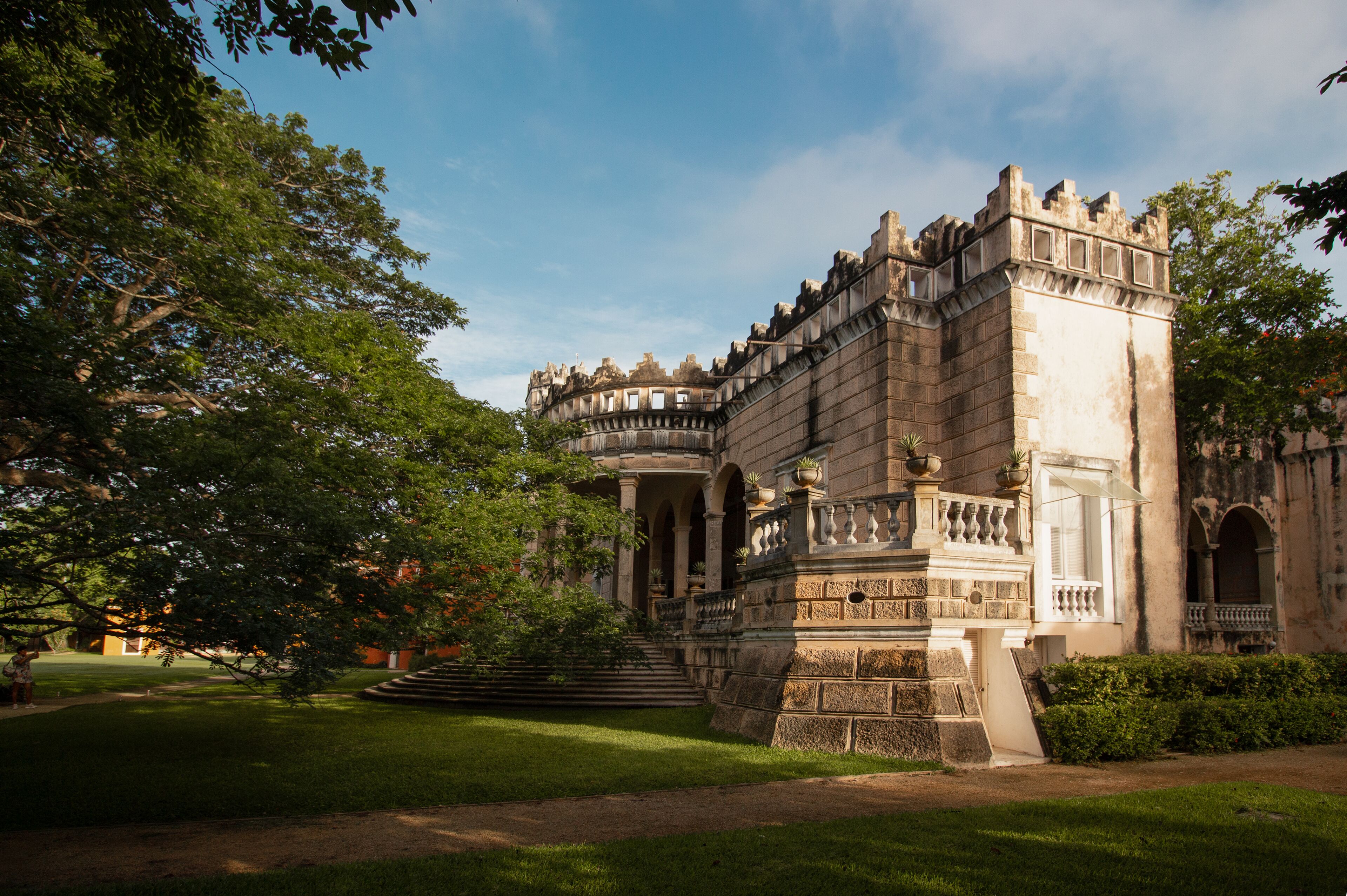 A historic building with a grand entrance, a well-maintained garden, and a clear sky.