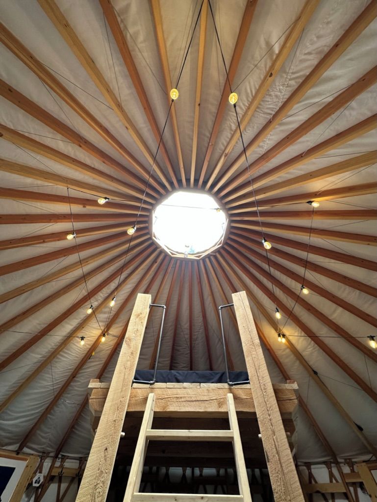 Una habitación con techo alto, vigas de madera, tragaluces y lámparas colgantes.