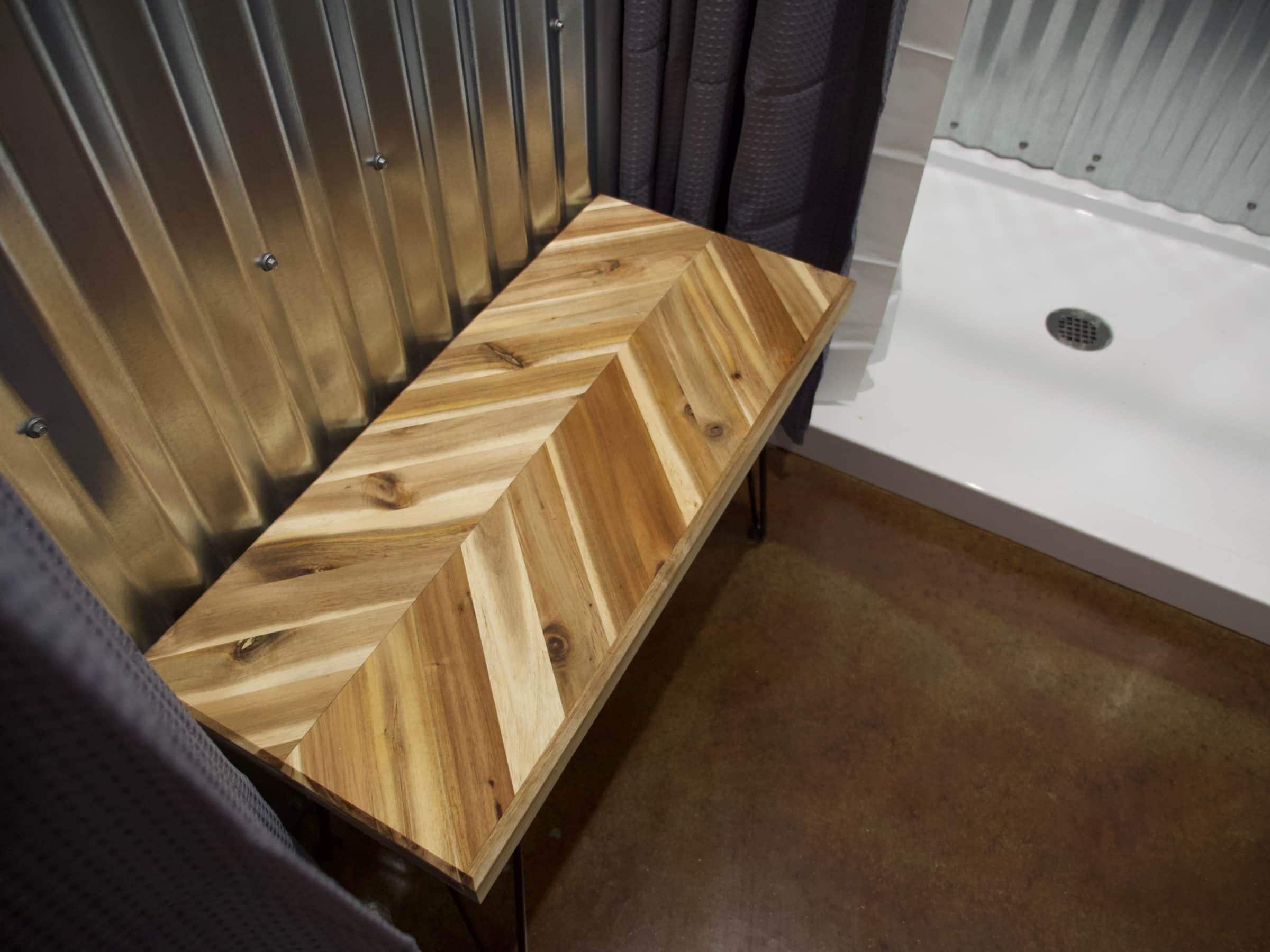 Un banco de madera con diseño de patrón en chevron en un baño con bañera blanca y ducha.