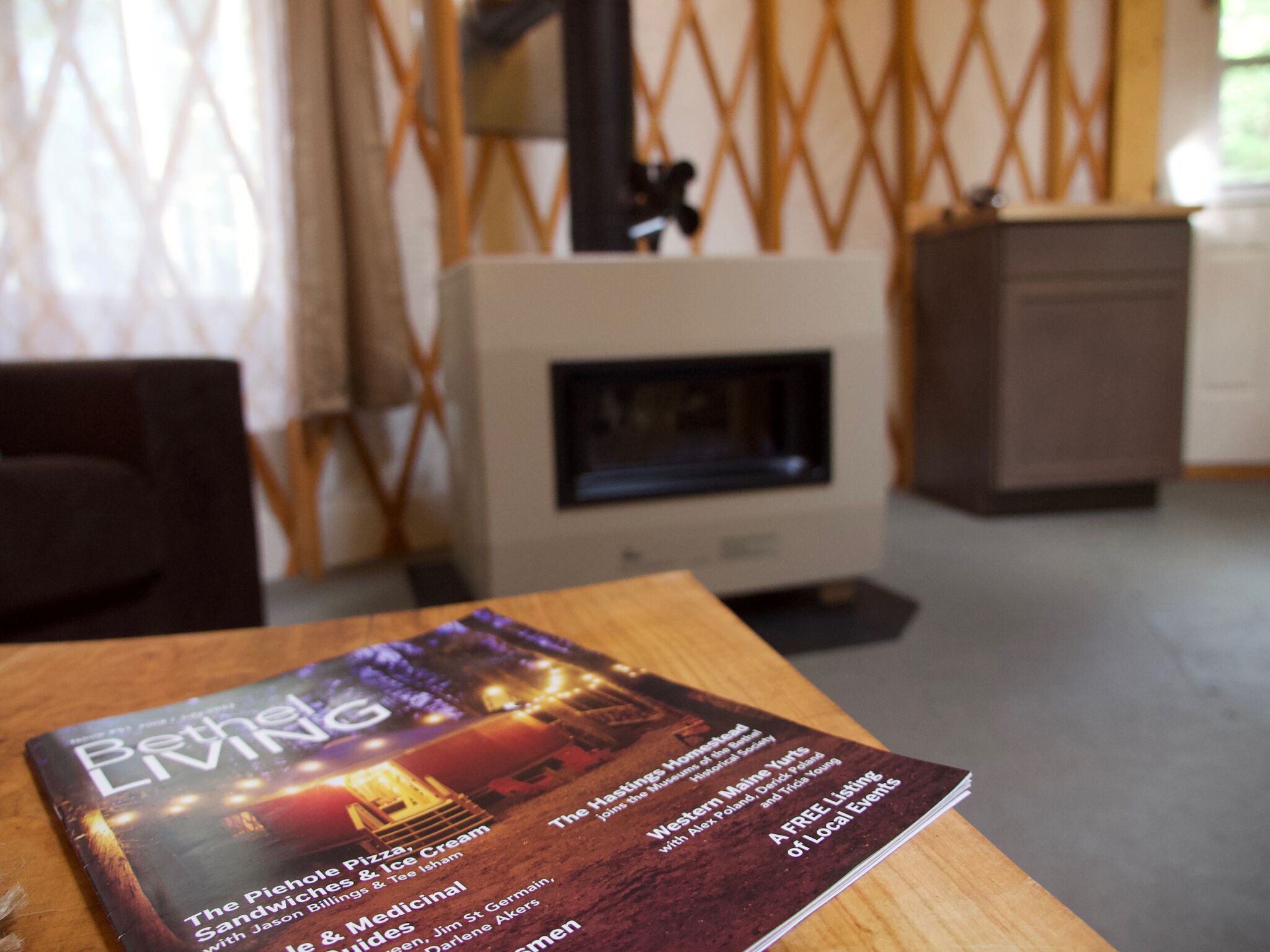 Une brochure intitulée « Beth Living » est posée sur une table en bois dans une pièce dotée d’une cheminée, d’un mur à motifs et d’une armoire.
