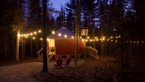 Un chalet confortable avec un toit en forme de dôme, entouré d’arbres, et doté d’une petite véranda avec des chaises.
