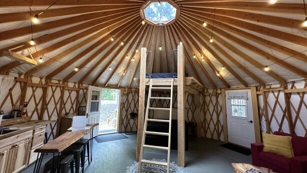 Een tent met houten inrichting, een centrale ladder, een eethoek en een knus zitgedeelte.