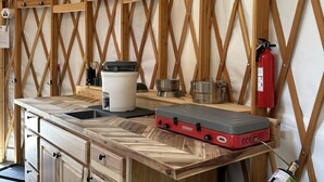 Een rustieke keuken met houten balken, een spoelbak, kastjes, een draagbaar fornuis en een brandblusser.