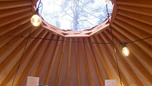 Een gezellig interieur van een houten joert met een rond dakraam, een bed met kussen, en lichtjes.