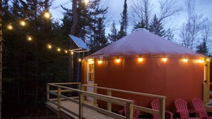 A wooden deck leading to a red yurt with string lights, surrounded by trees. - The Swift Glamping Yurt in Western Maine (Bethel)