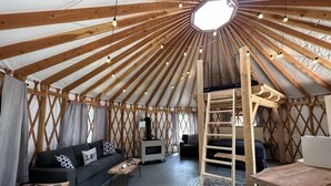 A yurt interior with a central wooden ladder, a sofa, a small table, and a TV. - The Swift Glamping Yurt in Western Maine (Bethel)