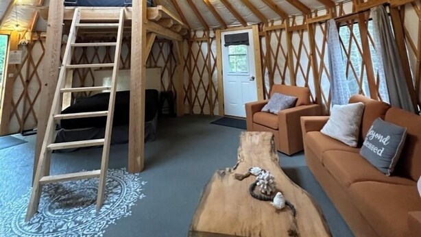L’intérieur d’une yourte, avec une échelle en bois, un canapé, une table basse et une porte.